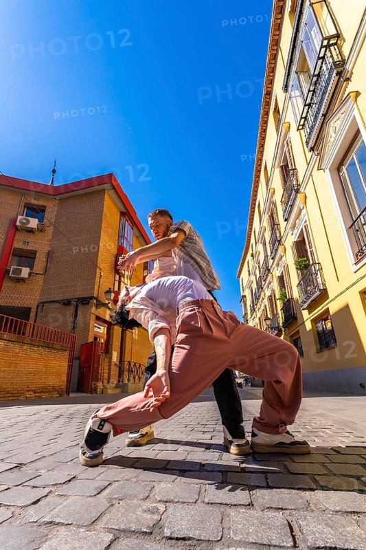 Two skilled dancers engaging in a passionate contemporary performance on a cobblestone street, expressing movement and connection in an urban environment with traditional buildings