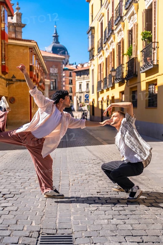 Two young men expressing emotion and movement through a modern dance routine on a cobblestone street, performing in an urban setting with historic architecture