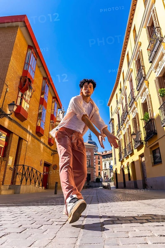 Young man striking a dynamic urban dance pose on sunlit cobblestones in madrid, radiating energy, style and carefree expression against historic city architecture
