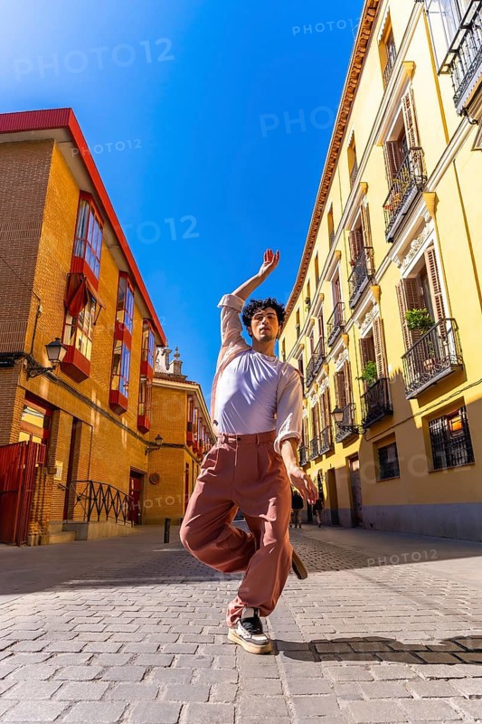 Young man creating art with his body, dancing ballet street style in an urban environment, expressing freedom and joy in the middle of a city street on a sunny day