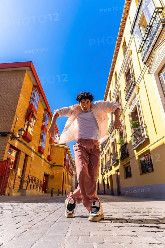 Stylish young man with intense expression executing a dynamic street dance move on cobblestones in a vibrant european city district, full length, sunny, energetic summer scene