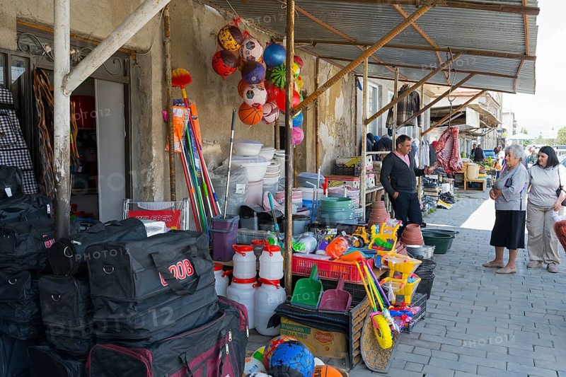 A shopping street with toys and household goods, meat hanging in front of the door, customers looking at the goods, Martuni, Gegharkunik province, Armenia