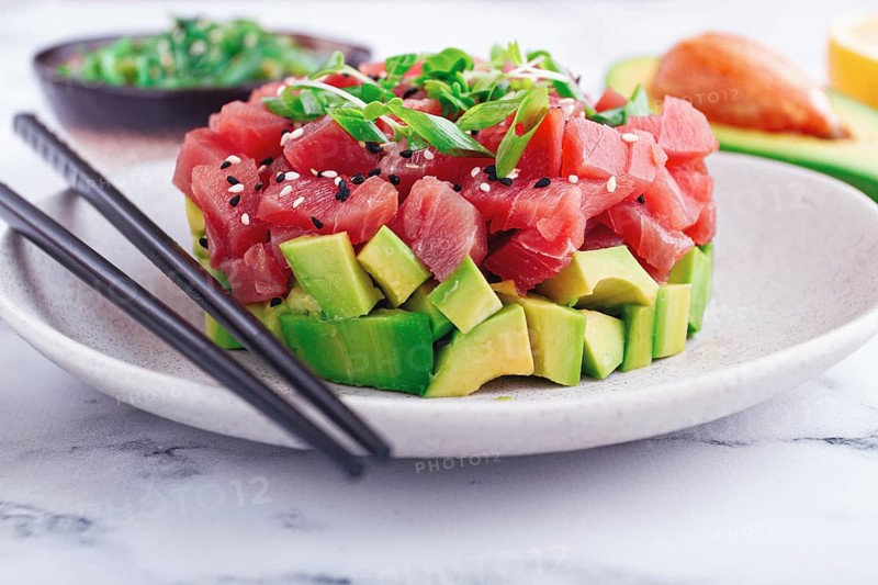 Fresh tuna tartare with avocado served on a marble table with soy sauce and seaweed salad