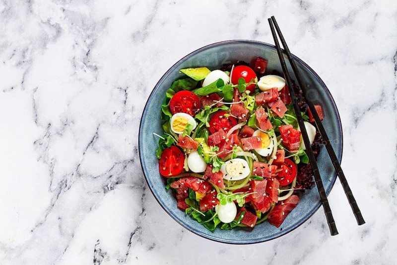 Salad with fresh tuna, cherry tomatoes and quail eggs and avacado, served with chopsticks