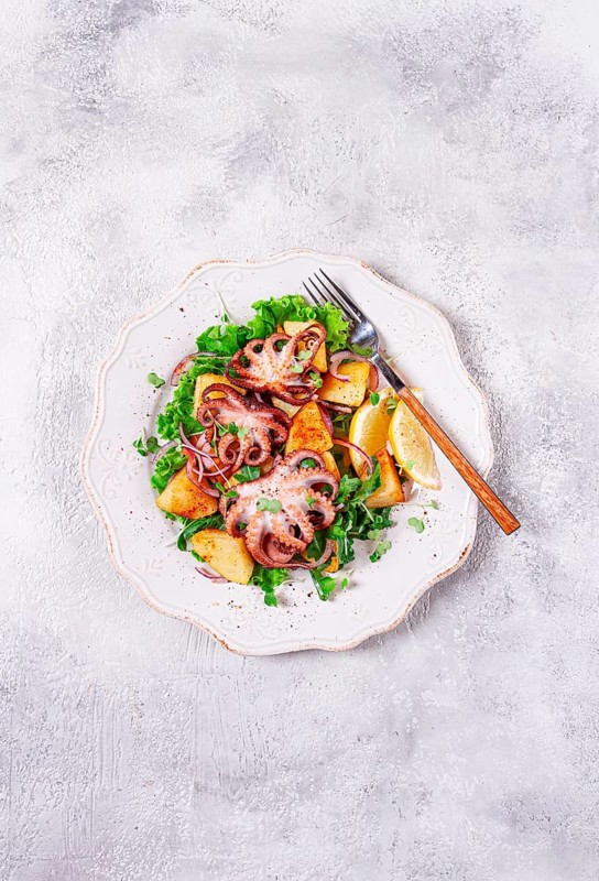 Grilled octopus with baked potatoes and fresh herbs, on a decorative light plate, homemade, no people