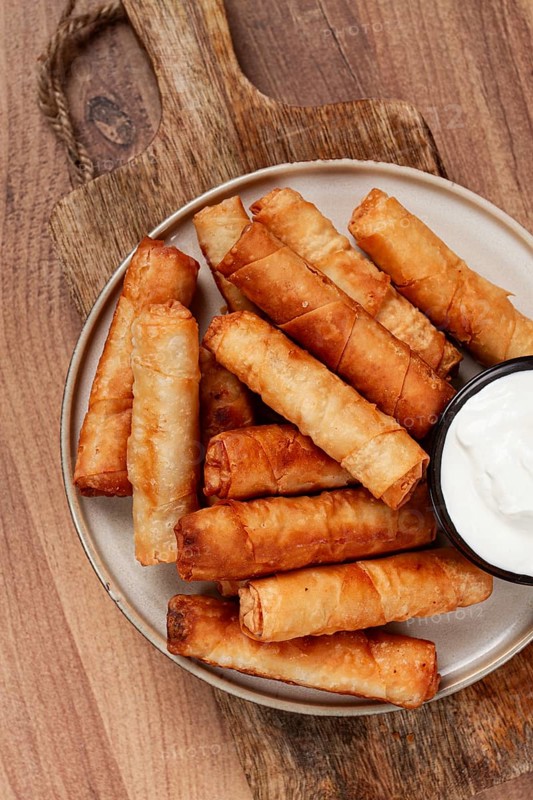 Fried spring rolls with cheese, on a wooden background, with cream sauce, no people