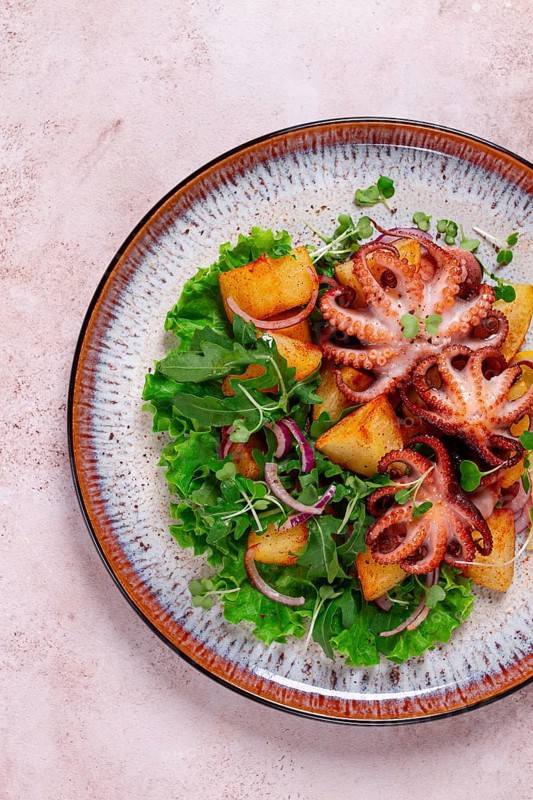 Grilled octopus with baked potatoes and fresh herbs, on a decorative plate, homemade