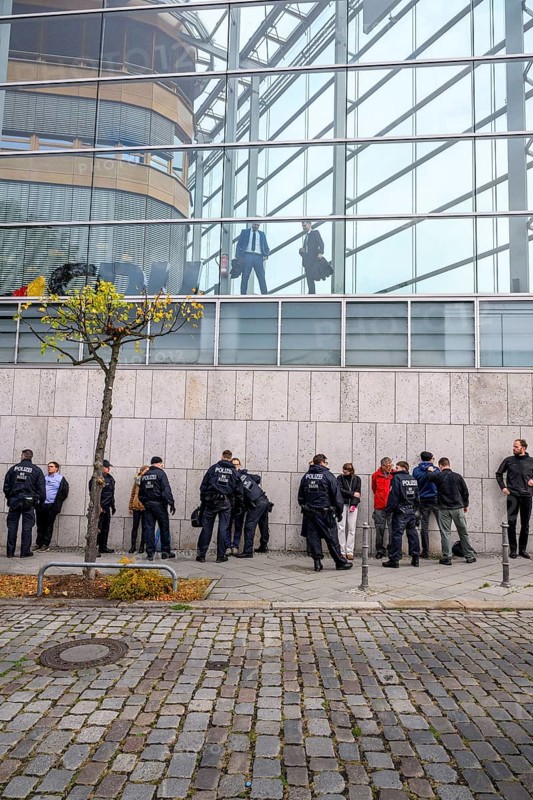 Men look out of the Konrad Adenauer House. Below, police detain activists of the New Generation. After an attempt at a performance by the New Generation to fight corruption in front of the Konrad Adenauer House, the federal headquarters of the CDU. Berlin, 06.10.2025