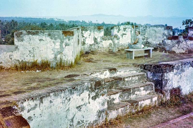 British expatriate tourist woman sitting on bench by walls ruin thought to be Malacca or Melaka, Malaya, Malaysia, south east Asia c 1964