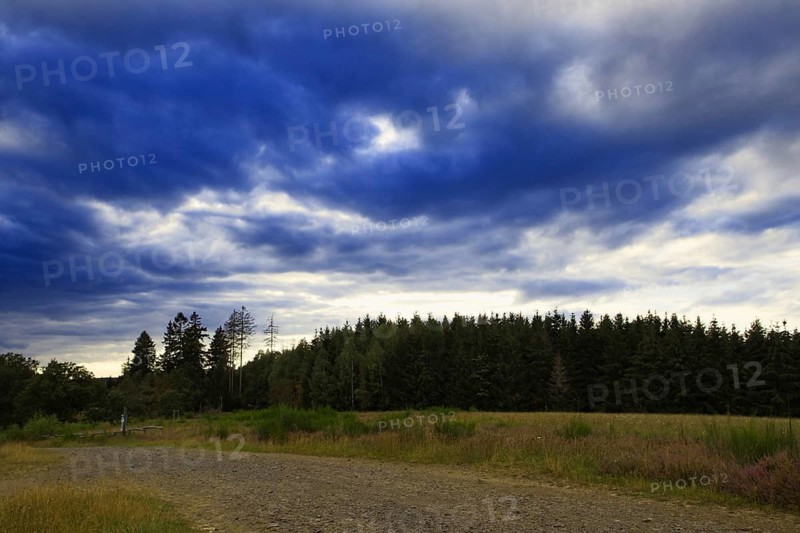 Dramatic sky with dark clouds over a field and neighbouring forest, heaths and rough grassland nature reserve near Trupbach, Siegen