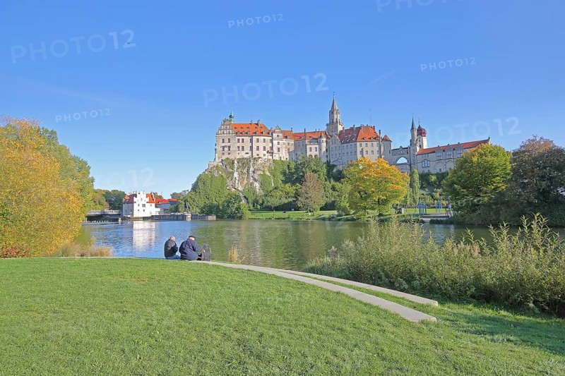 Hohenzollern Castle and Danube, river bank with autumn colours and two seated people, landmark, castle, Sigmaringen, Swabian Alb, Baden-Württemberg, Germany