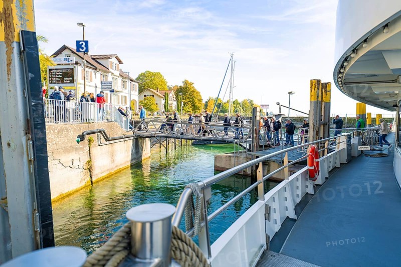 View from the ferry deck to the shore with waiting passengers and autumn foliage, Meersburg, Lake Constance, Germany