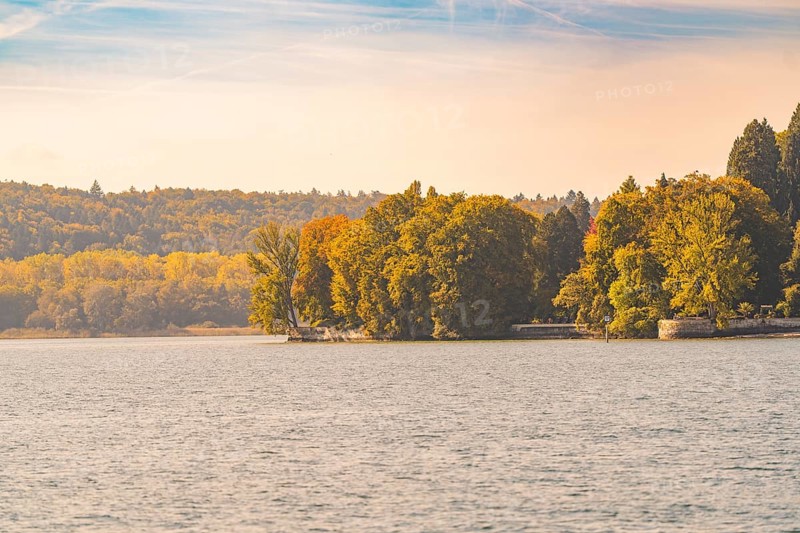 Autumnal shoreline with trees and calm lake, Mainau Island, Lake Constance, Germany