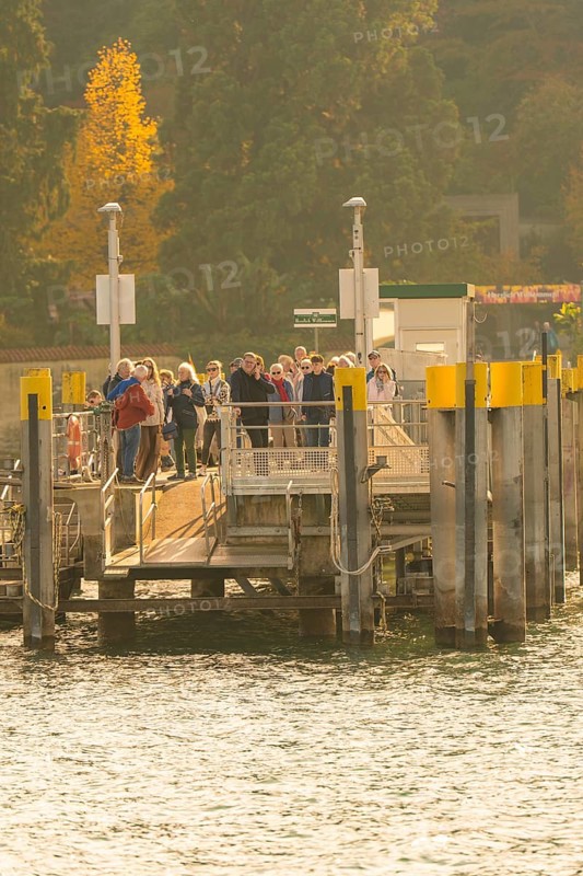 People waiting at a jetty surrounded by trees with autumn colours, Mainau Island, Lake Constance, Germany