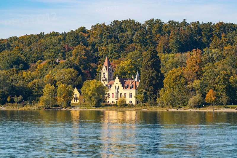 A picturesque castle on the shore of a lake surrounded by autumnal trees with a clear sky, Constance, Lake Constance, Germany