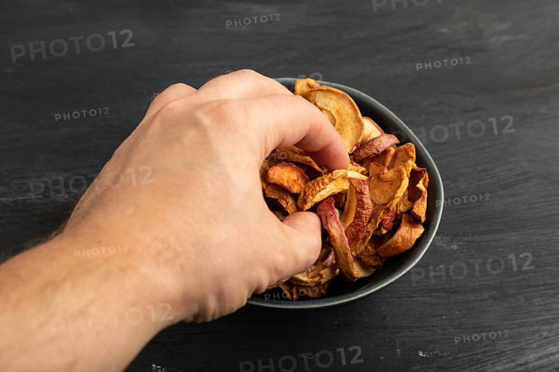 Dried Apples in ceramic bowl with hand on black wooden background. Side view, close up. healthy food, minimalism. sweet hold