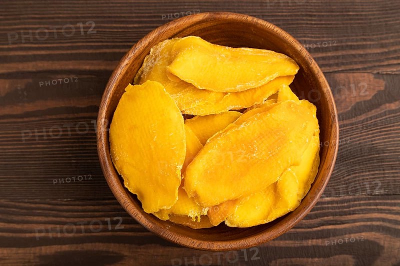 Dried Mango in wooden bowl on brown wooden background. Top view, close up, flat lay. healthy food, minimalism