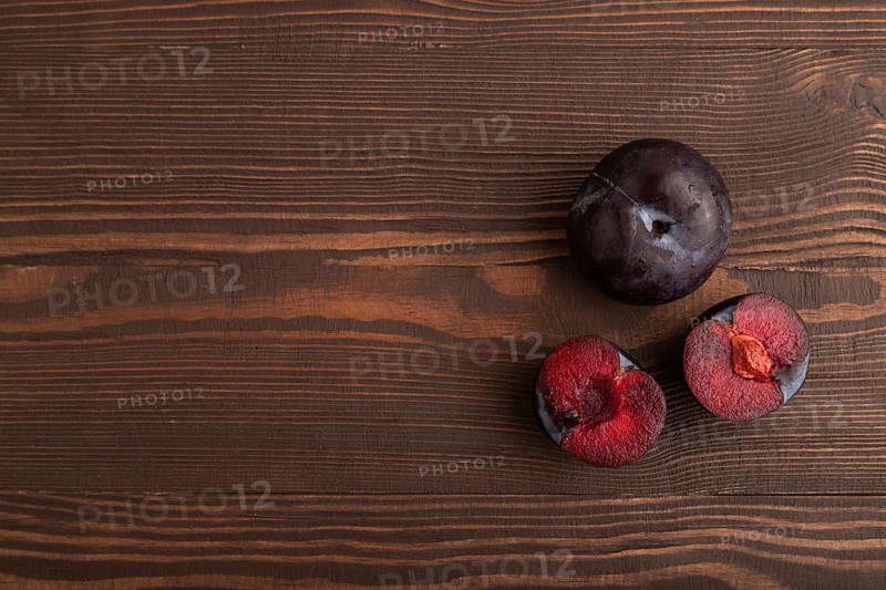 Purple Plum Cut in half on brown wooden background. Top view, flat lay, copy space. healthy food, vegetable, minimalism