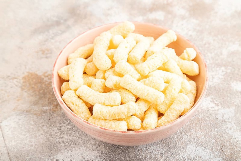 Corn flakes sticks with caramel in ceramic bowl on gray concrete background. Side view, close up