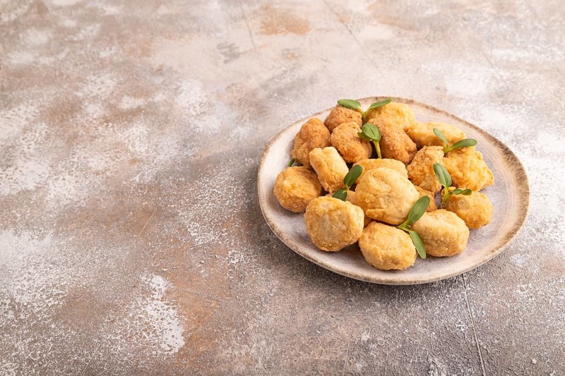 Fried crispy Chicken Nuggets with ketchup, microgreen on brown concrete background. side view, copy space