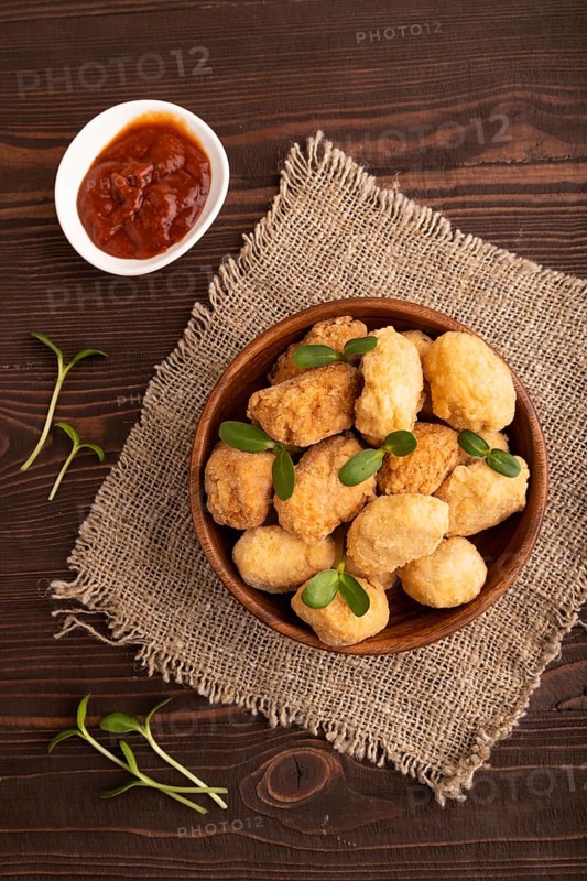 Fried crispy Chicken Nuggets with ketchup, microgreen on brown wooden background and linen textile. top view, flat lay, close up