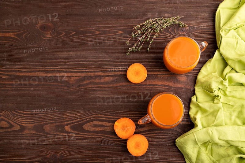 Two glasses with carrot juice, on wooden background and green textile. Diet, healthy eating concept. top view, flat lay, copy space, minimalism