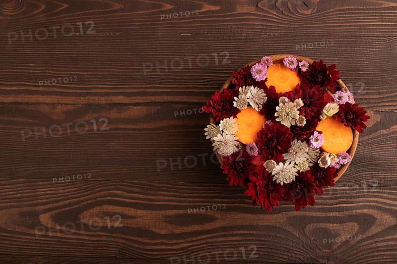 Wooden bowl with carrot slices and red Chrysanthemum flowers, Astrantia flowers, flower salad on brown wooden background, top view, flat lay, copy space, minimalism
