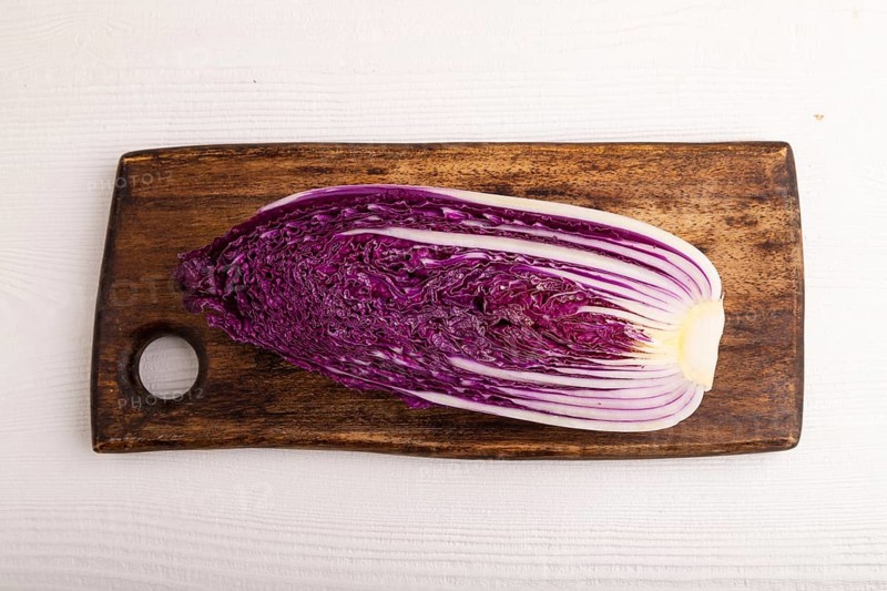 Purple Chinese cabbage on cutting board on white wooden background, top view, flat lay, close up, minimalism
