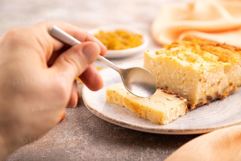?ottage cheese ?asserole, Curd cake, with dried apricots and raisins with hand on brown concrete background and orange textile, side view, selective focus, minimalism