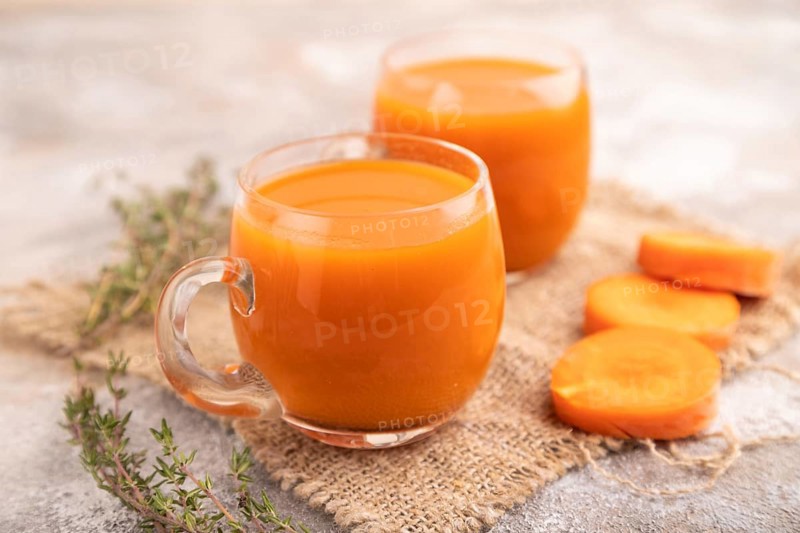 Two glasses with carrot juice, on brown concrete background and linen textile. Diet, healthy eating concept. side view, close up, minimalism, selective focus