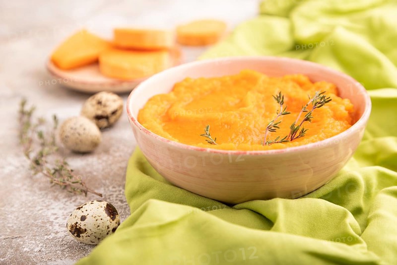 Sweet potato porridge in ceramic bowl on brown concrete background and green textile. Diet, healthy eating concept. side view, close up, selective focus