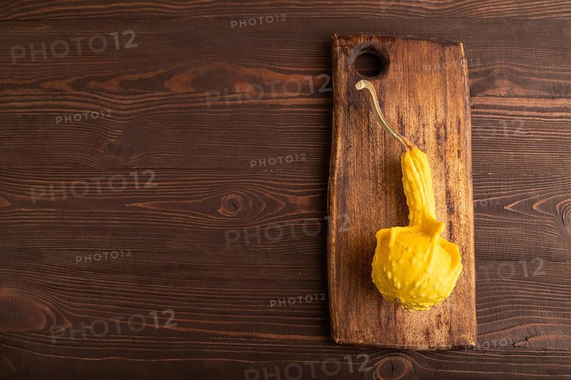 Decorative orange Pumpkin on cutting board on brown wooden background, top view, flat lay, copy space, minimalism