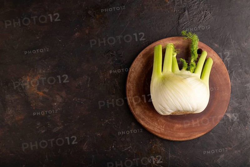Fresh Fennel bulb on wooden cutting board on black concrete background, top view, flat lay, copy space, minimalism