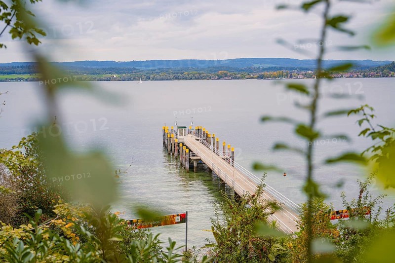 View of a long jetty leading into a calm lake with a cloudy sky in the background, Mainau Island, Lake Constance, Germany