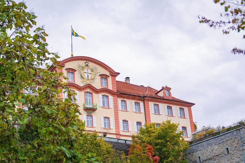 A magnificent building with a flag in the foreground, surrounded by autumnal greenery, Mainau Island, Lake Constance, Germany