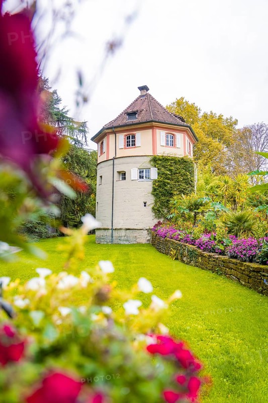 Tower-like building surrounded by flowering garden and green meadow, Mainau flower island, Lake Constance, Germany