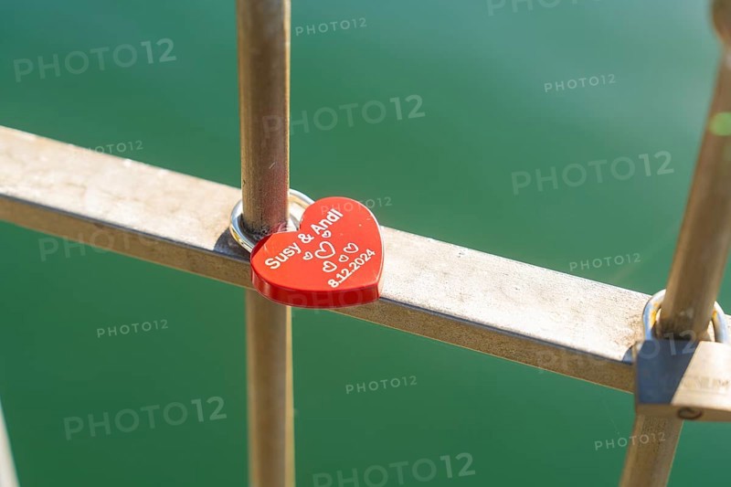Red heart lock with engraving on the railing over green water, Überlingen, Lake Constance, Germany
