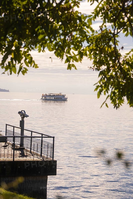 A boat passes by on a calm lake, visible from a binocular viewpoint next to a jetty, Überlingen, Lake Constance, Germany