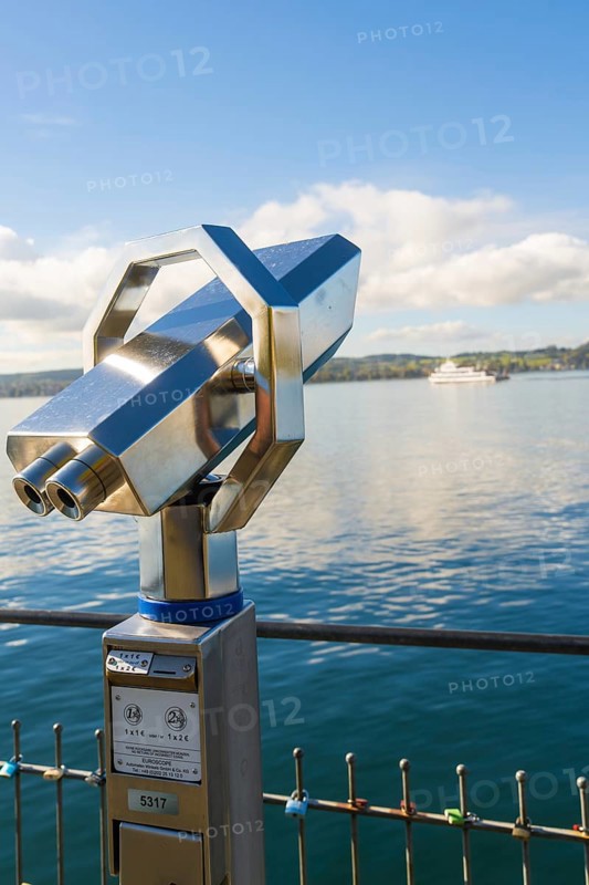 Binoculars on the shore with a ship in the background on the calm lake, Überlingen, Lake Constance, Germany