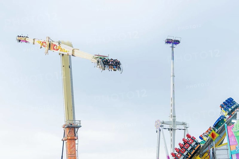 View of thrill rides with people high above and other attractions in the background, Cannstatter Wasen funfair, Stuttgart, Germany