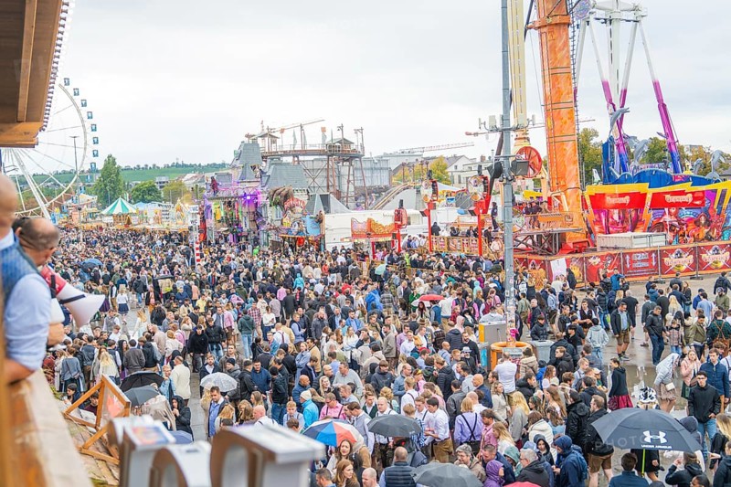 Large crowd at a folk festival with fairground rides under a cloudy sky, Cannstatter Wasen folk festival, Stuttgart, Germany