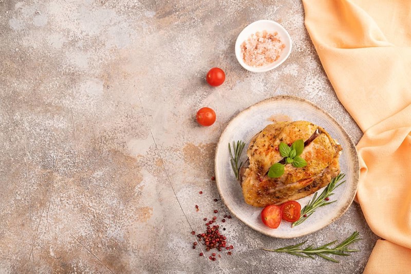 Fried Turkey Thigh with spices and rosemary on plate on brown concrete background and orange linen textile. top view, flat lay, copy space