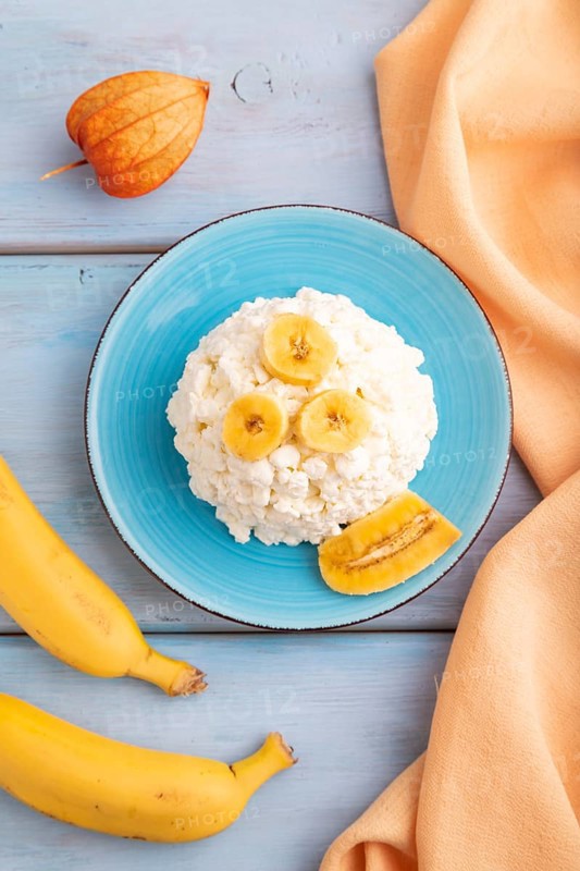 White ?ottage cheese, Curd, with Banana on blue wooden background and orange textile, top view, flat lay, close up