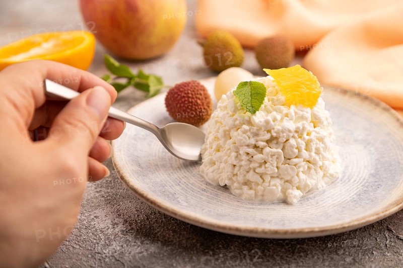 White ?ottage cheese, Curd, with orange and lychee with hand on brown concrete background and orange textile, side view, close up, selective focus