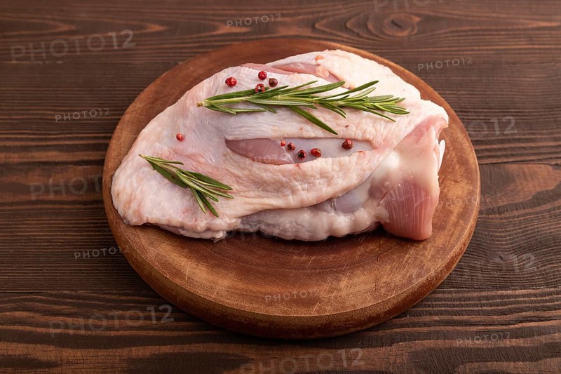 Raw Turkey Thigh with spices and rosemary on cutting board on brown wooden background. side view, close up