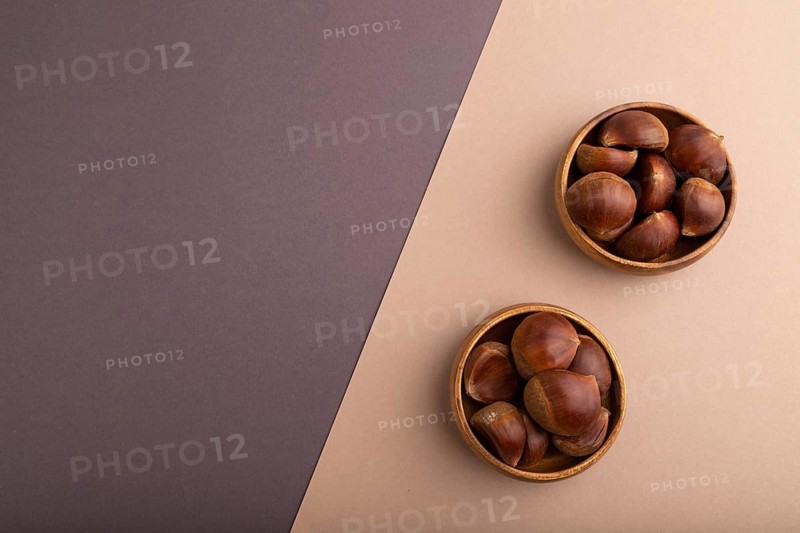 Wooden bowl with raw edible ?hestnuts on brown and gray paper pastel background, top view, flat lay, copy space, minimalism