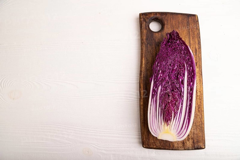 Purple Chinese cabbage on cutting board on white wooden background, top view, flat lay, copy space, minimalism