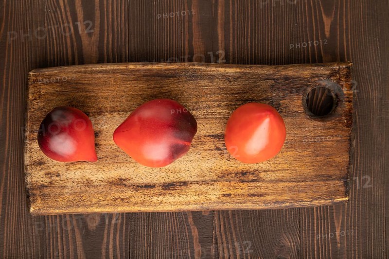 Red Heart shape tomatoes on cutting board on brown wooden background. Top view, copy space, flat lay. healthy food, vegetable, minimalism