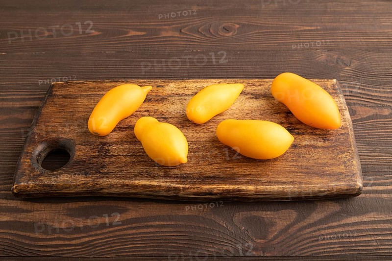 Yellow tomatoes on cutting board on brown wooden background. Side view, copy space. healthy food, vegetable, minimalism