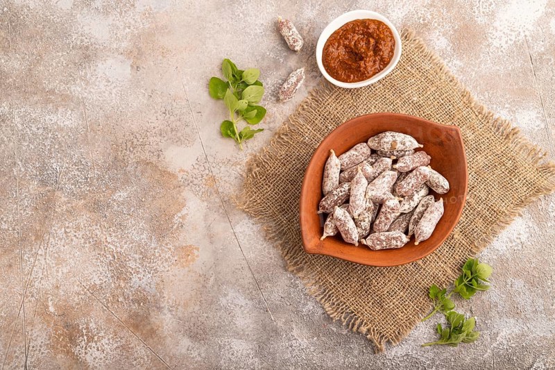Small smoked Chicken sausages in clay bowl on brown concrete background and linen textile. top view, flat lay, copy space